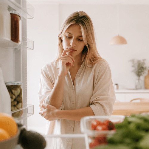 Frau im Alltag, die unter Mental Load steht und Schwierigkeiten hat, sich regelmäßig und gesund zu ernähren. Helle, natürliche Darstellung von Frauengesundheit, Ernährung, Stress und Alltagsbelastung. Symbolische Darstellung dafür, wie Erschöpfung, Decision Fatigue und mentale Last gesunde Ernährung im Alltag beeinflussen.
