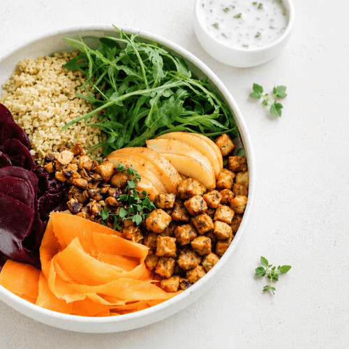 Pflanzenbasierte Rote-Bete-Hirse-Bowl mit Kichererbsen, Rucola, frischen Kräutern und cremigem Dressing in einer hellen Schüssel auf einem minimalistischen Küchentisch.
