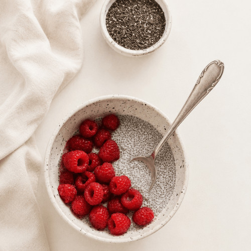 Ballaststoffreiche Lebensmittel wie Vollkornbrot, Haferflocken, Leinsamen, Chiasamen und Himbeeren auf einer hellen Arbeitsplatte.