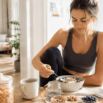 Darmflora für Frauen: Dein Darm gehört auf Deine Selfcare-Liste Frau beim Frühstück mit Haferflocken, Beeren, Nüssen und fermentiertem Gemüse zur Unterstützung der Darmflora.
